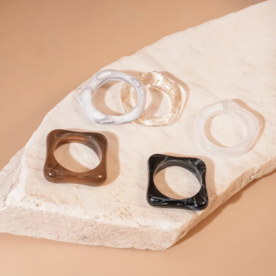 5pc smudged acrylic fashion rings set in white marble, gold-speckled clear, translucent clear, brown, and black.