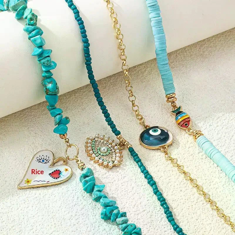 Three turquoise and gold beaded bracelets with decorative charms, including a heart charm with 'Rice' text, a pearl heart charm, and an evil eye charm, displayed on a textured white surface | DIVINE TIMES by Shopp Java