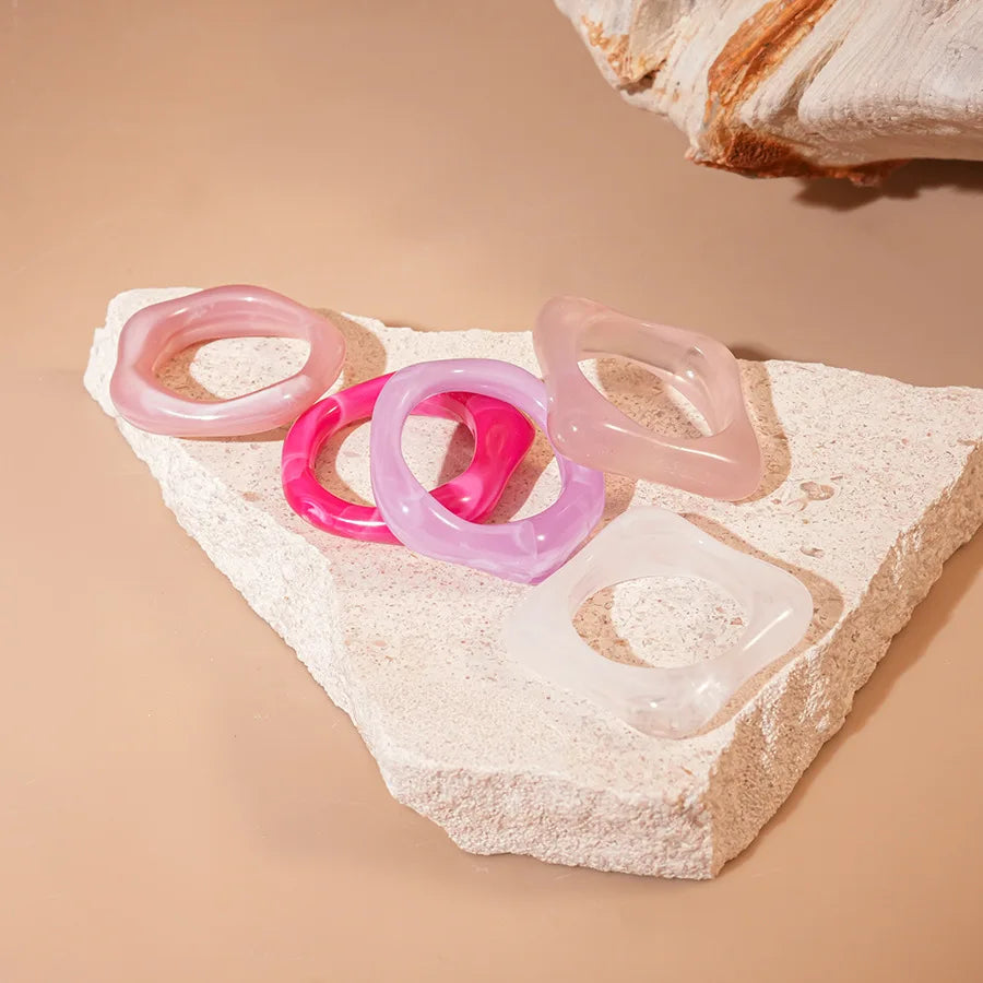 5pc set of smudged acrylic fashion rings in pastel pink, purple, and clear on a stone block